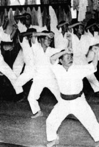 Gichin Funakoshi beim Training an einer Tokyoter Uni. Zum Trocknen aufgehängte Karateanzüge im Hintergrund.